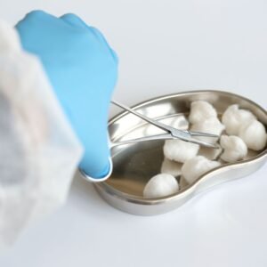 Close-up of latex gloved hand using forceps to handle cotton balls in a kidney dish.